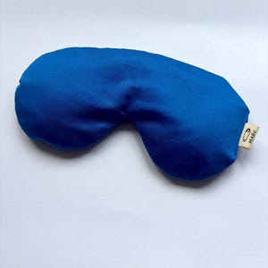 May include: A solid royal blue sleep mask with a smooth, satin-like finish. The mask features a small, light beige fabric tag on the right side, which displays a black safety pin icon and the text MARV printed in a clear, sans-serif font.