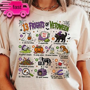 May include: A cream-colored t-shirt featuring a graphic titled 13 FRIGHTS OF VETOWEEN. The design displays thirteen numbered illustrations related to veterinary work with Halloween themes, including a ghost, unpaid bills, a cat in a witch hat, spilled samples, a pumpkin, a vaccine, a puppy, intestinal parasites, an x-ray, a blood bag, a magnifying glass with a flea, a pet carrier, and nail clippers.
