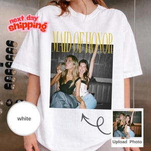 May include: White t-shirt with a photo print featuring two women and the text "MAID OF HONOR" in gold. The shirt also has a small photo and the words "Upload Photo".