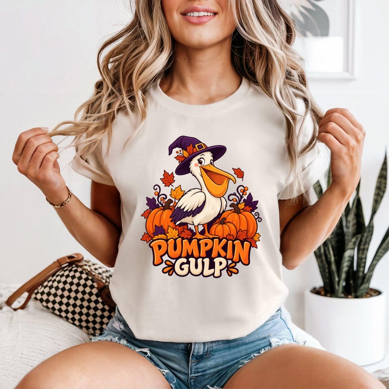 A whimsical illustration of a pelican wearing a purple witch hat, surrounded by orange pumpkins and autumn leaves, with the text PUMPKIN GULP in bold glossy orange letters. — shown on a ivory product
