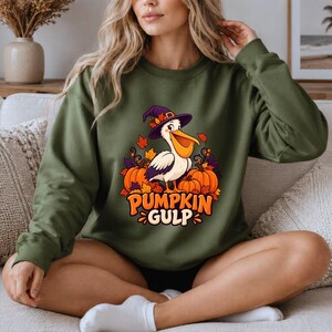 A whimsical illustration of a pelican wearing a purple witch hat, surrounded by orange pumpkins and autumn leaves, with the text PUMPKIN GULP in bold glossy orange letters.