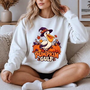 A whimsical illustration of a pelican wearing a purple witch hat, surrounded by orange pumpkins and autumn leaves, with the text PUMPKIN GULP in bold glossy orange letters. — shown on a white product