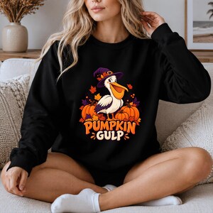 A whimsical illustration of a pelican wearing a purple witch hat, surrounded by orange pumpkins and autumn leaves, with the text PUMPKIN GULP in bold glossy orange letters. — shown on a black product
