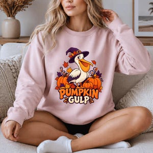 A whimsical illustration of a pelican wearing a purple witch hat, surrounded by orange pumpkins and autumn leaves, with the text PUMPKIN GULP in bold glossy orange letters.