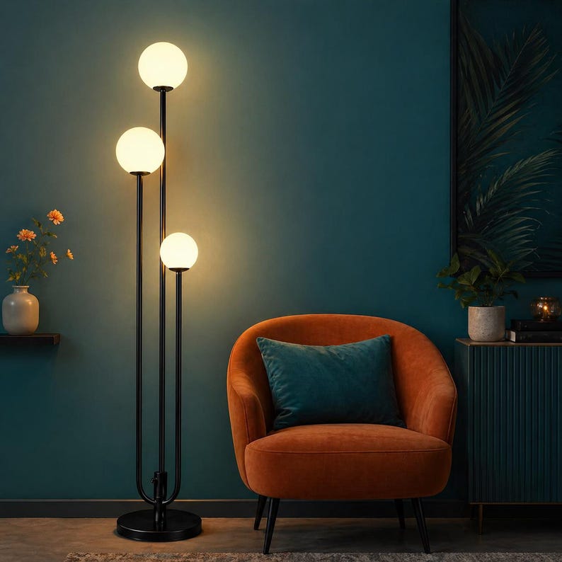 May include: A black floor lamp with three spherical, white glass shades. The lamp is positioned next to an orange armchair with a teal pillow. The background is a dark teal wall.