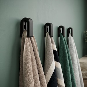 Könnte beinhalten: Vier Handtücher hängen an schwarzen Wandhaken. Die Handtücher sind in Beige-, Grau- und Grüntönen gehalten. Die Haken sind an einer grünen Wand befestigt. Die Handtücher scheinen aus einem weichen, saugfähigen Material zu bestehen.