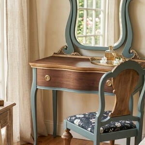 May include: A vanity table with a natural wood top and a single drawer, featuring a blue-painted frame and legs. An attached mirror with a blue frame and gold accents sits on top. A matching chair with a blue frame and a black floral seat cushion.