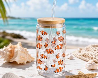 Puede incluir: Un vaso de cristal transparente con tapa de bambú y pajita de cristal, que presenta un patrón repetitivo de peces payaso naranjas y blancos. El vaso cilíndrico tiene una boca ancha y está decorado con múltiples ilustraciones de peces.