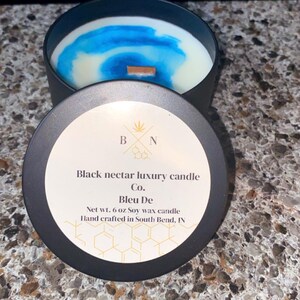 May include: A black candle tin with a lid, containing a soy wax candle with blue and white swirls. The lid is labelled "Black nectar luxury candle Co. Bleu De" and "Net wt. 170 g Soy wax candle".