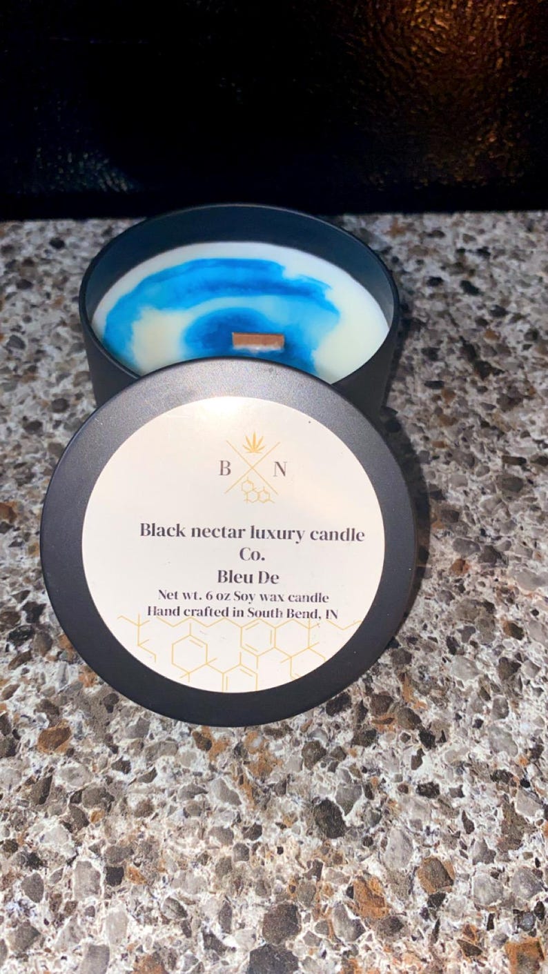 May include: A black candle tin with a lid, containing a soy wax candle with blue and white swirls. The lid is labelled "Black nectar luxury candle Co. Bleu De" and "Net wt. 170 g Soy wax candle".