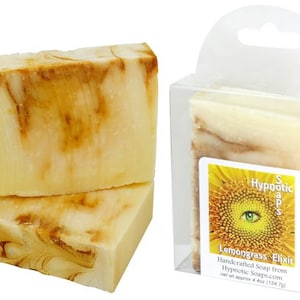 Op de afbeelding: Twee handgemaakte zeepjes met lemongrasselixir, een op de ander, in een doorzichtige plastic verpakking met een etiket waarop staat "Hyppotic Soaps Lemongrass Elixir Handcrafted Soap from Hypnotic Soaps.com net at approx 4 oz (124.7g)"