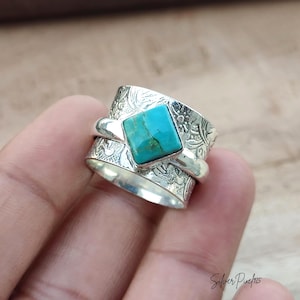 May include: A wide silver spinner ring featuring a central square turquoise stone with dark veining. The band has an intricate embossed floral pattern across the surface. The text Silver Pixel 925 is visible in the bottom right corner.