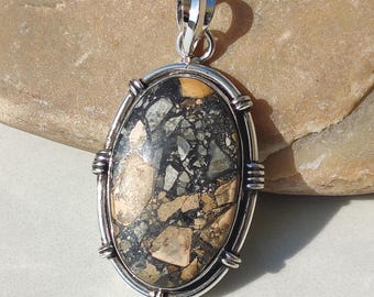 May include: Oval pendant with a silver-colored frame. The pendant features a mosaic of black, gray, and tan stones. The bail is a silver-colored loop. The pendant is a unique piece of jewelry.