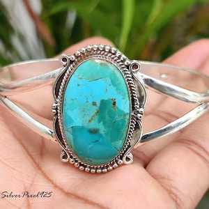 Peut inclure: Un bracelet manchette en argent orné d'une grande pierre ovale turquoise. La pierre est d'un bleu-vert vif avec des motifs naturels. Le bracelet a un sertissage orné et une finition polie. Le texte "Silver Pixel925" est visible.
