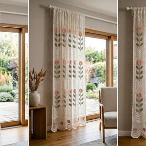 Puede incluir: Un panel de cortina de encaje color crema con un patrón vertical repetitivo de flores rosas bordadas con tallos y hojas verdes. La tela tiene una textura delicada de tejido abierto con un borde inferior festoneado y cuelga de una barra.