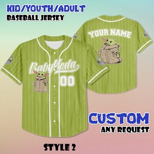 Puede incluir: Camiseta de b&eacute;isbol verde con rayas blancas, con "Baby Yoda" y el n&uacute;mero "00" en la parte delantera. La parte trasera de la camiseta tiene "YOUR NAME" impreso sobre un gr&aacute;fico de Baby Yoda. La camiseta est&aacute; etiquetada como "STYLE 2" y "CUSTOM ANY REQUEST".