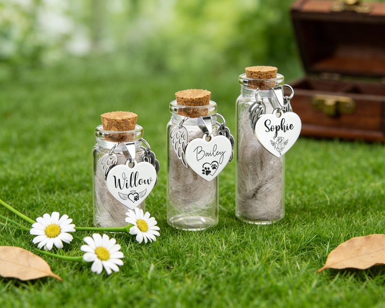 May include: Three small glass bottles with cork stoppers, each containing a fluffy substance. Each bottle has a silver heart-shaped charm with a name engraved on it: Willow, Bailey, and Sophie. The bottles are on green grass.