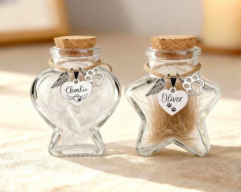 May include: Two clear glass keepsake jars with cork stoppers. One is heart-shaped, the other star-shaped. Each jar has a silver charm with a name and paw print. The heart jar says "Charlie", the star jar says "Oliver".