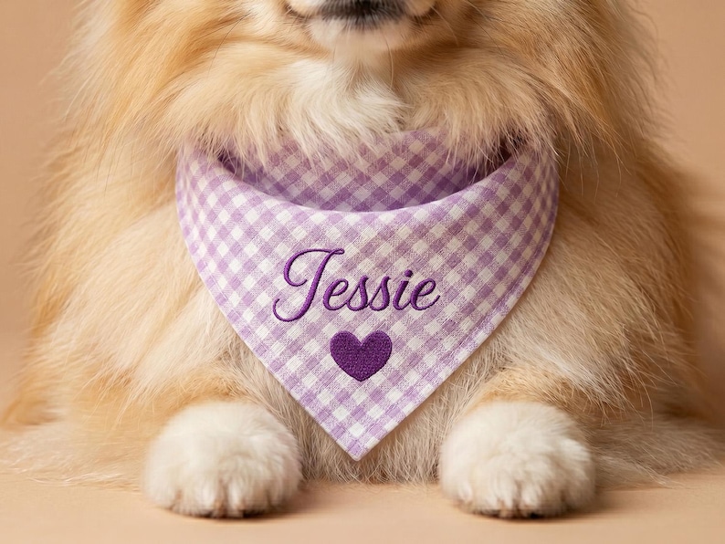 May include: A triangular pet bandana featuring a light purple and white gingham check pattern. The fabric is embroidered with the name Jessie in a dark purple cursive script, positioned directly above a solid dark purple heart icon.