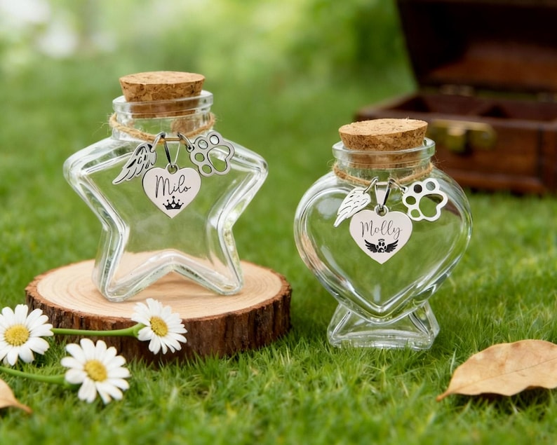 May include: Two clear glass keepsake jars with cork stoppers. One is star-shaped, the other heart-shaped. Each has a charm with a name and paw print. The star jar says "Milo", the heart jar says "Molly". Both sit on a wooden slice.