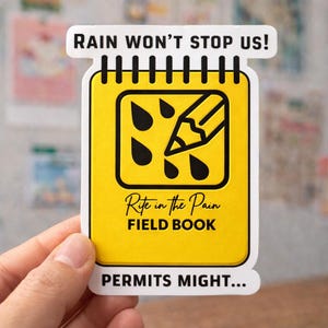 May include: A yellow sticker in the shape of a notepad with the text "RAIN WON'T STOP US!" at the top and "PERMITS MIGHT..." at the bottom. The notepad design includes a pencil and raindrops, with the words "Rite in the Pain FIELD BOOK".