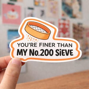 Może przedstawiać: Wycięta naklejka z pomarańczową i białą obwódką. Naklejka przedstawia ilustrację sita oraz tekst "YOU'RE FINER THAN MY No.200 SIEVE" w kolorze czarnym i pomarańczowym. Naklejka jest trzymana w dłoni.