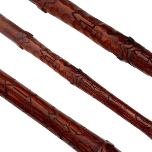 Puede incluir: Primer plano de tres varitas de madera talladas intrincadamente. Las varitas son de un color marrón oscuro intenso con patrones y texturas detalladas. El diseño incluye formas geométricas talladas y pequeñas secciones elevadas.