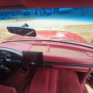 Può includere: Vista interna del cruscotto rosso di un'auto. Il cruscotto, il volante e la moquette sono tutti in una tonalità rosso intenso. Uno schermo nero è montato al centro e uno specchietto retrovisore è appeso al parabrezza. Gli interni dell'auto sono ben tenuti.