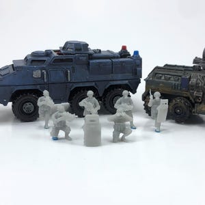 May include: Miniature military vehicles and soldiers. The image features two armored vehicles, one blue and one green, with several small, gray soldier figurines. The vehicles have detailed designs, and the soldiers are in various poses, suggesting a battle scene.