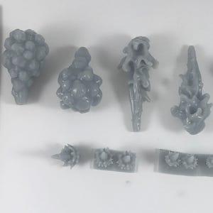 May include: A collection of gray resin miniatures, including various organic shapes and a mushroom-like figure. A ruler with inch measurements is in the frame. The miniatures appear to be for a tabletop game or model.