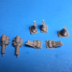 May include: A collection of small, gray plastic model parts, including what appear to be miniature engines and other mechanical components. The parts are arranged on a solid blue background.