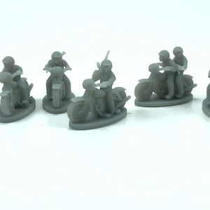 Puede incluir: Colección de pequeñas figuras de motocicletas grises. Algunas figuras representan un solo motorista, mientras que otras muestran dos. Una figura tiene un motorista sosteniendo un rifle. Las motocicletas tienen detalles, como faros y asientos. Las figuras están sobre bases ovaladas.