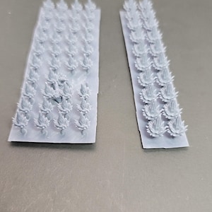 May include: Two light gray, rectangular sheets with numerous small, stylized flame-like shapes. The shapes are arranged in rows and columns, suggesting a repeating pattern. The sheets are placed on a gray surface.