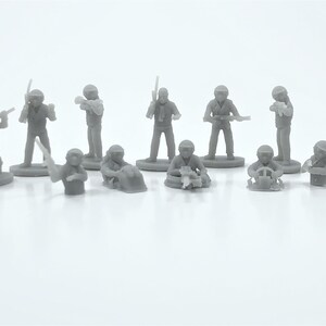 Puede incluir: Un conjunto de pequeñas figuras de plástico gris que representan soldados en diversas poses de acción. Algunas figuras están de pie y sostienen armas, mientras que otras están arrodilladas o sentadas. Las figuras están sobre bases circulares, posiblemente de un juego.