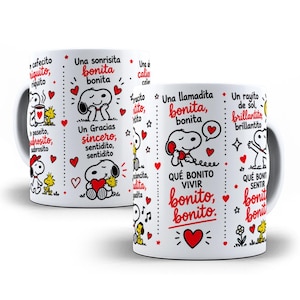 May include: A white ceramic mug featuring Snoopy and Woodstock illustrations with red and black Spanish text including phrases like Una sonrisita bonita, Una llamadita bonita, and Qué bonito vivir bonito, accented by numerous small red hearts and stars.