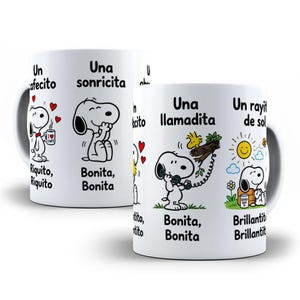Puede incluir: Una taza de cerámica blanca con ilustraciones de Snoopy y texto en español. Las escenas muestran a Snoopy con una taza de café, sonriendo, hablando por teléfono con Woodstock y sentado junto a un sol. El texto incluye Un cafecito, Una sonricita, Una llamadita y Un rayito de sol.