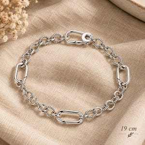 May include: A silver chain bracelet featuring a mix of textured rope-style circular links and smooth elongated oval links. The bracelet includes a secure clasp mechanism stamped with 925 and measures 19 cm in total length as indicated.