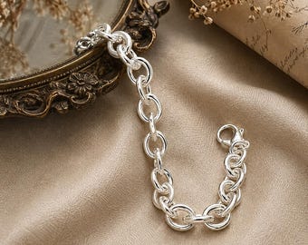 Può includere: Un bracciale a catena in argento lucido caratterizzato da una serie di maglie circolari uniformi e arrotondate collegate tra loro. Il bracciale include una chiusura a moschettone sicura a un'estremità, con una finitura metallica brillante e riflettente.