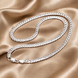 Op de afbeelding: Een zilverkleurige ketting met een klassiek gourmet schakelontwerp en een gepolijste, reflecterende afwerking. De ketting is voorzien van een veilige karabijnsluiting aan het uiteinde en toont een consistent, in elkaar grijpend metalen schakelpatroon.
