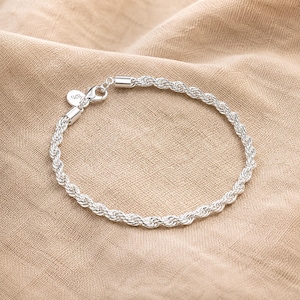 Könnte beinhalten: Ein silbernes Kordelkettenarmband mit gedrehtem Metalldesign und polierter Oberfläche. Das Armband verfügt über einen sicheren Karabinerverschluss und einen kleinen runden Anhänger mit der Prägung 925, die die Metallzusammensetzung angibt.