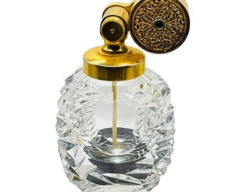 May include: A vintage perfume bottle with a clear, faceted glass body and a gold-colored metal atomizer. The atomizer features an ornate, circular design. The bottle has a classic, elegant aesthetic.