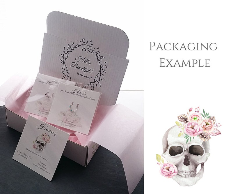 Puede incluir: Una caja blanca con el texto "Hello Beautiful!" y "Ready to rock?" impreso en la tapa interior. La caja contiene tarjetas de joyer&iacute;a y papel de seda rosa. Las tarjetas presentan dise&ntilde;os de joyas y tatuajes. Una ilustraci&oacute;n de calavera con flores est&aacute; a la derecha.