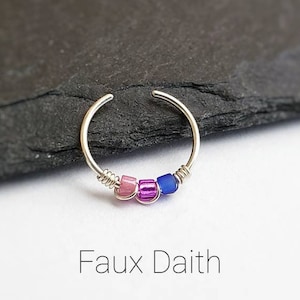 Puede incluir: Un pendiente falso daith de color plateado con tres peque&ntilde;as cuentas de colores. Las cuentas son rosas, moradas y azules. El pendiente tiene un dise&ntilde;o simple y circular. El texto "Faux Daith" est&aacute; debajo.