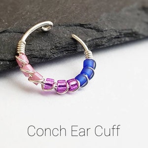 Puede incluir: Un pendiente de concha plateado con cuentas rosas, moradas y azules. El pendiente est&aacute; hecho de un alambre plateado que se enrolla alrededor de la oreja. El texto "Conch Ear Cuff" est&aacute; debajo.