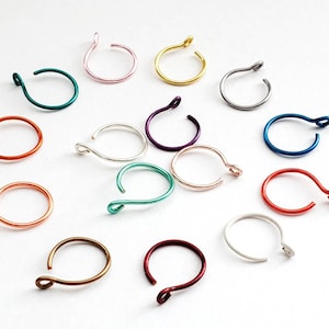 May include: Assortment of 14 colorful metal nose rings. The rings are made of wire and have a small loop at the end. The colors include pink, gold, silver, black, blue, green, red, and copper.