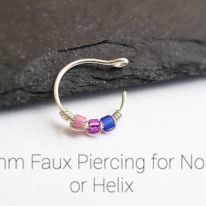 Puede incluir: Un piercing falso de nariz o h&eacute;lix de color plateado con tres peque&ntilde;as cuentas rosas, moradas y azules. El texto de la imagen dice "8mm Faux Piercing for Nose or Helix."
