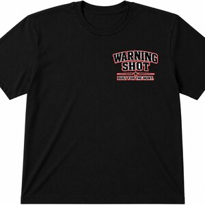Peut inclure: T-shirt noir avec l'inscription "WARNING SHOT" en rouge et blanc sur le haut de la poitrine gauche. En dessous, une étoile et les mots "BUILT FOR THE HUNT" en rouge.