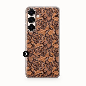 May include: A clear phone case featuring a brown and black lace pattern. The case has a rectangular shape with rounded corners and a camera module with three lenses. The lace design is intricate and covers the entire back of the case.