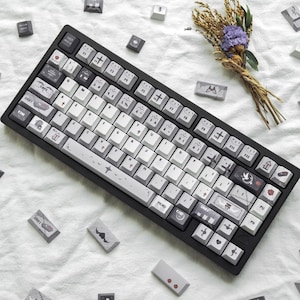 May include: A white ceramic mug with a black handle and the text "But First, Coffee" in a bold, black font. The mug is set against a blurred background, suggesting a cosy setting.