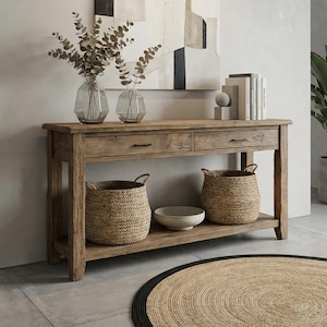 May include: A rectangular wooden console table with two drawers and a lower shelf. Two glass vases with eucalyptus branches, a set of books, and a small sphere sit on top. Two woven baskets and a white bowl are placed on the bottom shelf.
